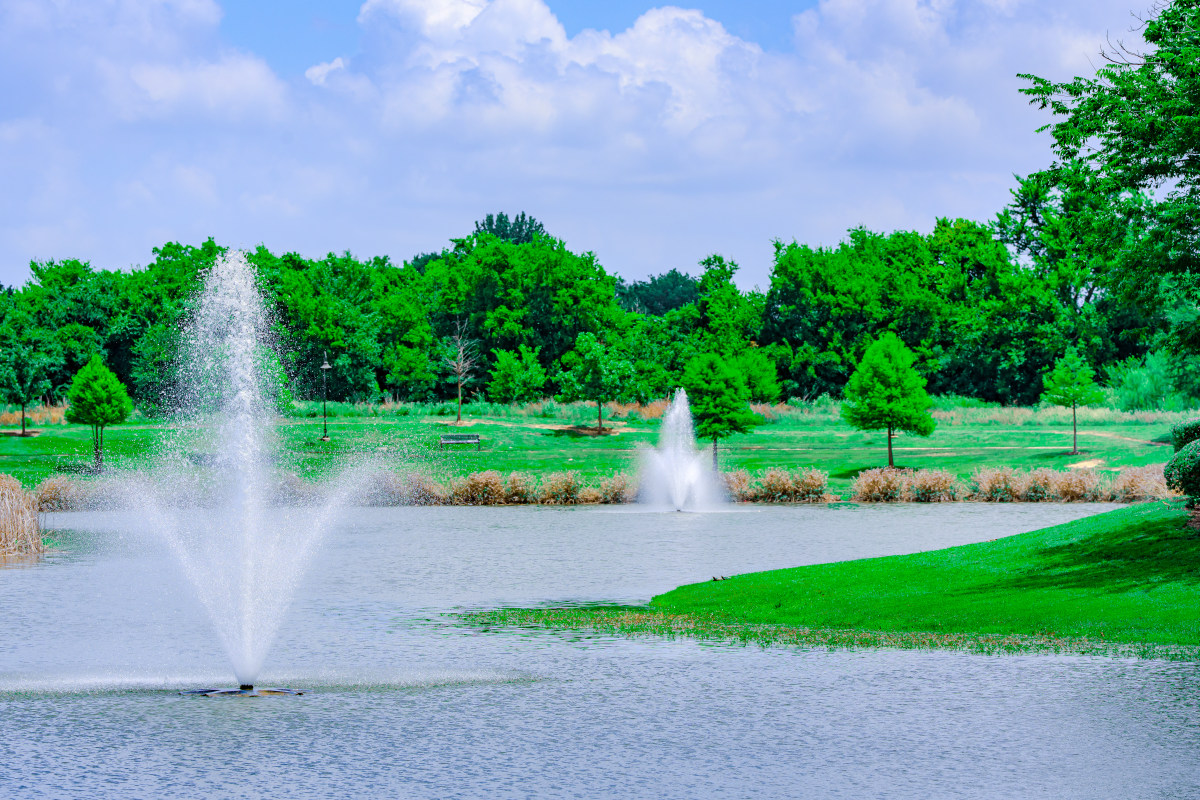 DSC05672 (1) Fountain spraying in the center of a grassy park area with trees in the distance